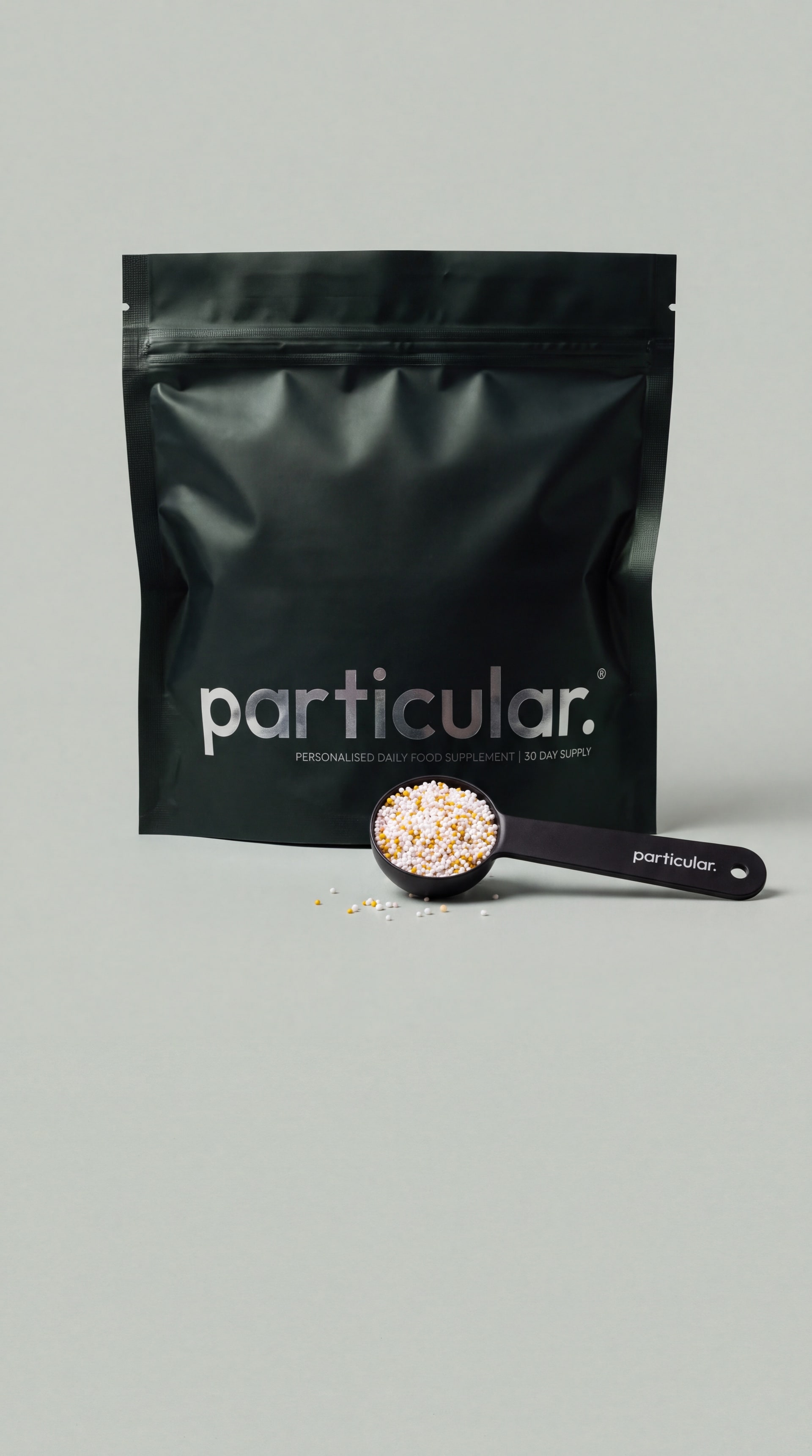 A Particular pouch on a pale stone plinth, beside a scoop filled with the daily microgranules
